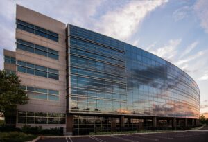 Modern curved glass and stone office building with horizontal window bands reflecting cloudy sky at sunset, featuring contemporary architecture design.