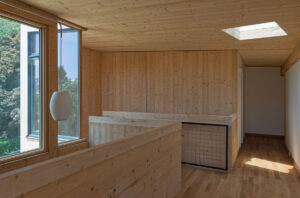 Modern wooden interior with large windows, skylight, and minimalist furnishings showcasing contemporary architectural design.