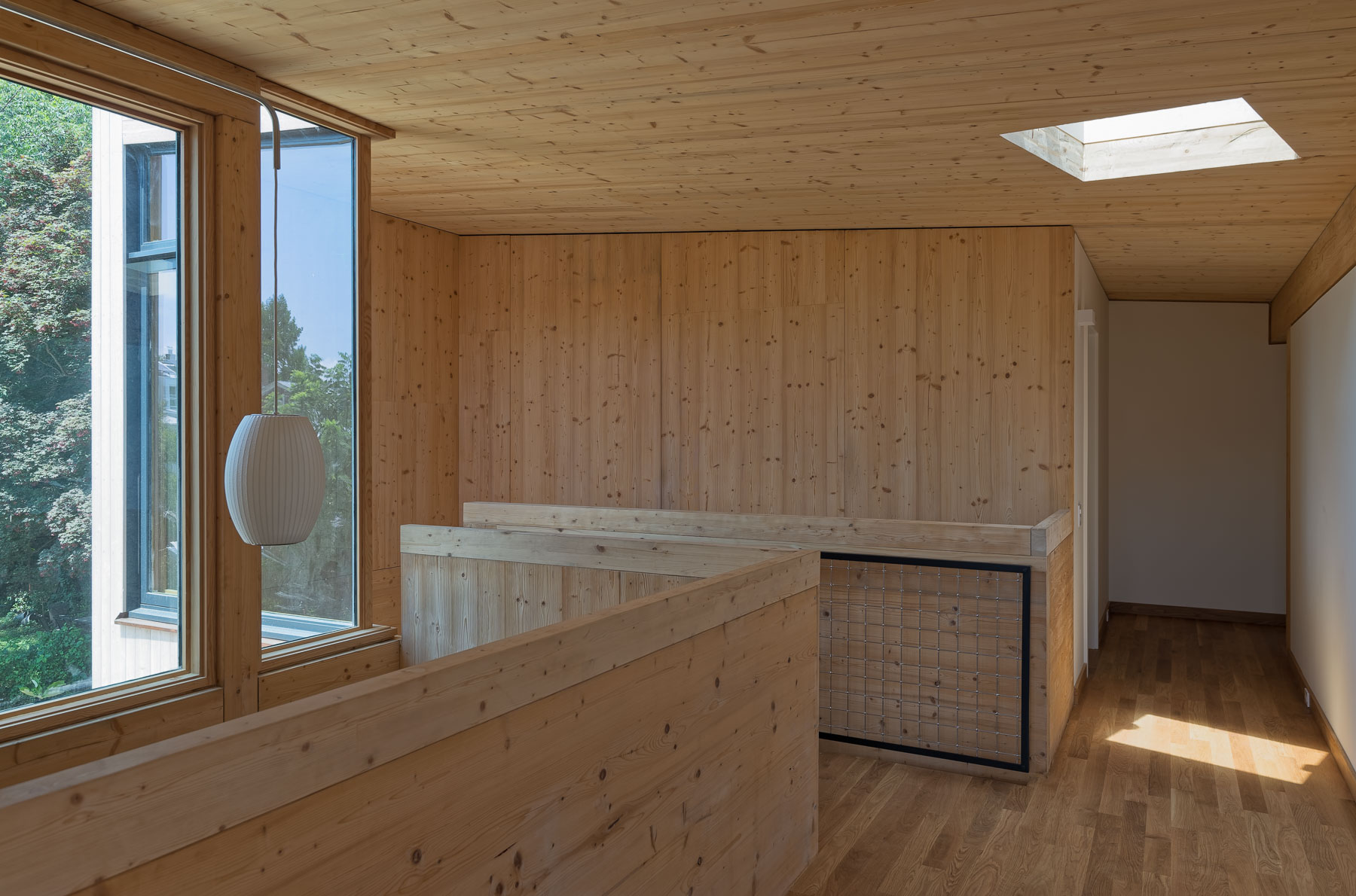 Modern wooden interior with large windows, skylight, and minimalist furnishings showcasing contemporary architectural design.