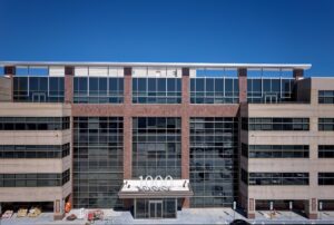 Modern multi-story commercial building with red brick facade, large glass windows, and rooftop signage against clear blue sky.