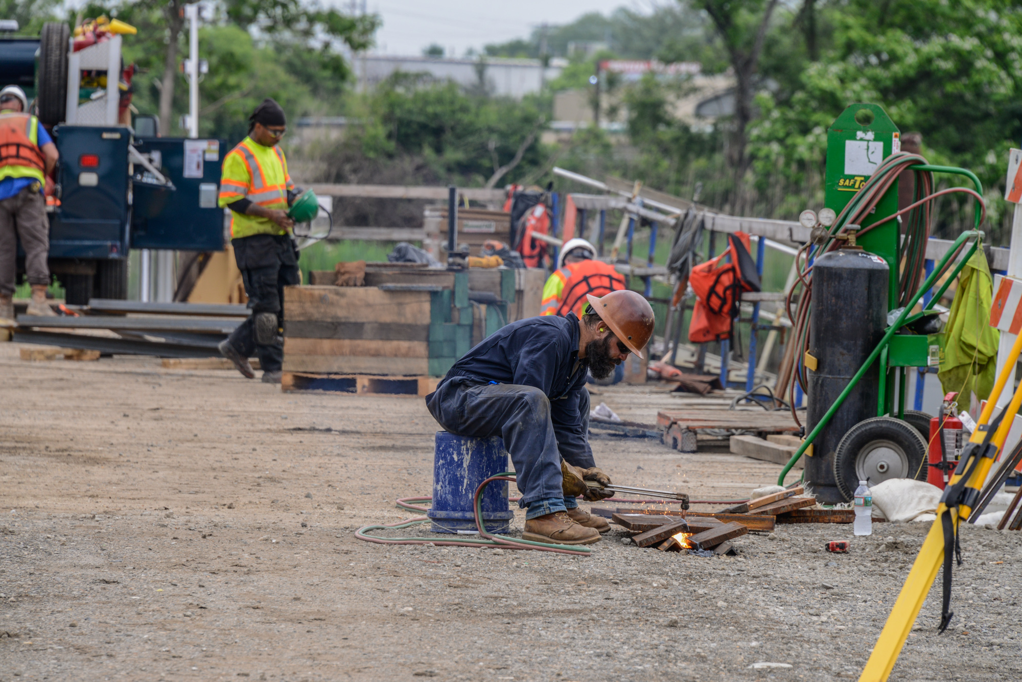 Construction worker welding metal pipes on industrial job site with equipment and machinery in background