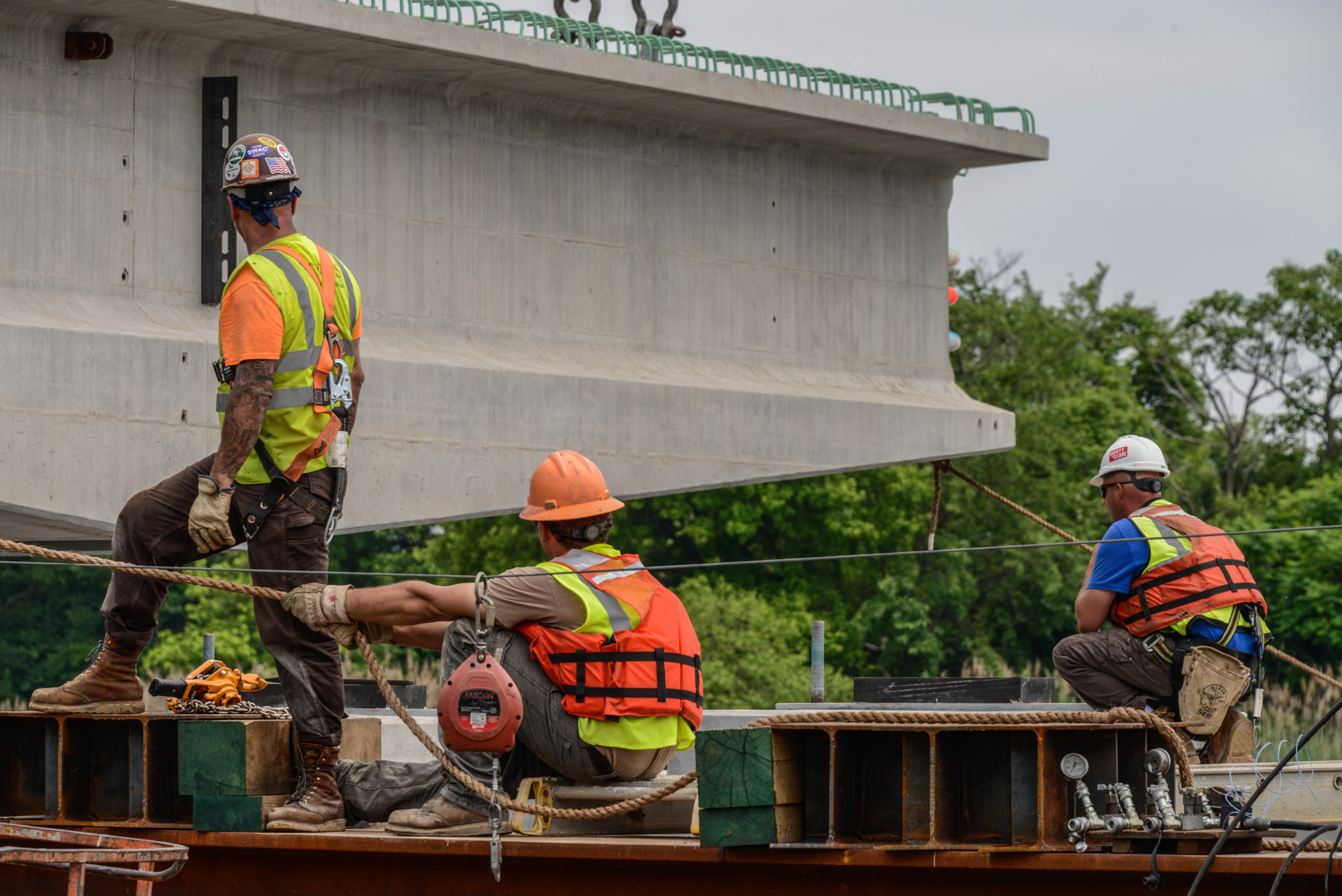 Three construction workers on scaffolding with safety equipment working on a concrete bridge structure during industrial construction project.