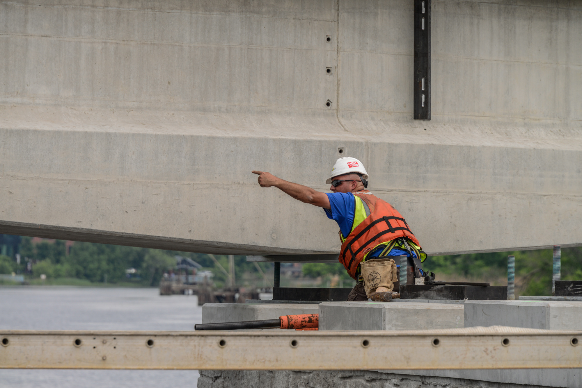 Construction worker in safety gear pointing at concrete structure during bridge inspection and industrial project documentation.