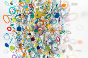 Vibrant abstract art installation featuring colorful geometric shapes, circles, and interconnected lines suspended against a white background.