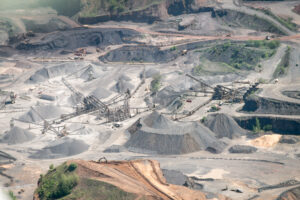Aerial view of active quarry mining operation with conveyor systems, stockpiles of crushed stone, and excavation equipment across multiple pit levels.