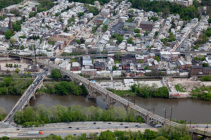 Aerial view of urban neighborhood with two bridges spanning a river, dense residential buildings, and highway traffic below.